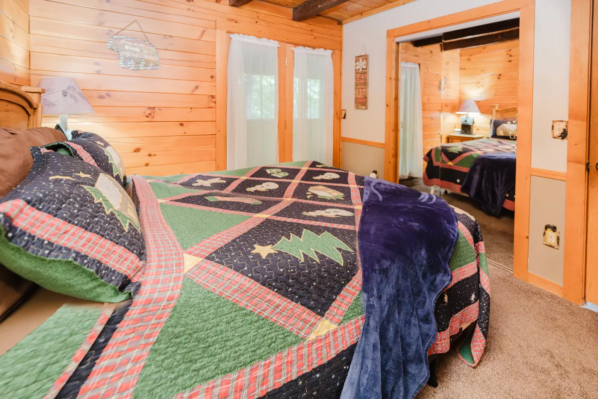 A snug bedroom with a quilted bedspread, rich wooden walls, and a sunlit window draped in sheer curtains. The room radiates warmth and tranquility, inviting couples to snuggle up, read, or enjoy a peaceful morning together.