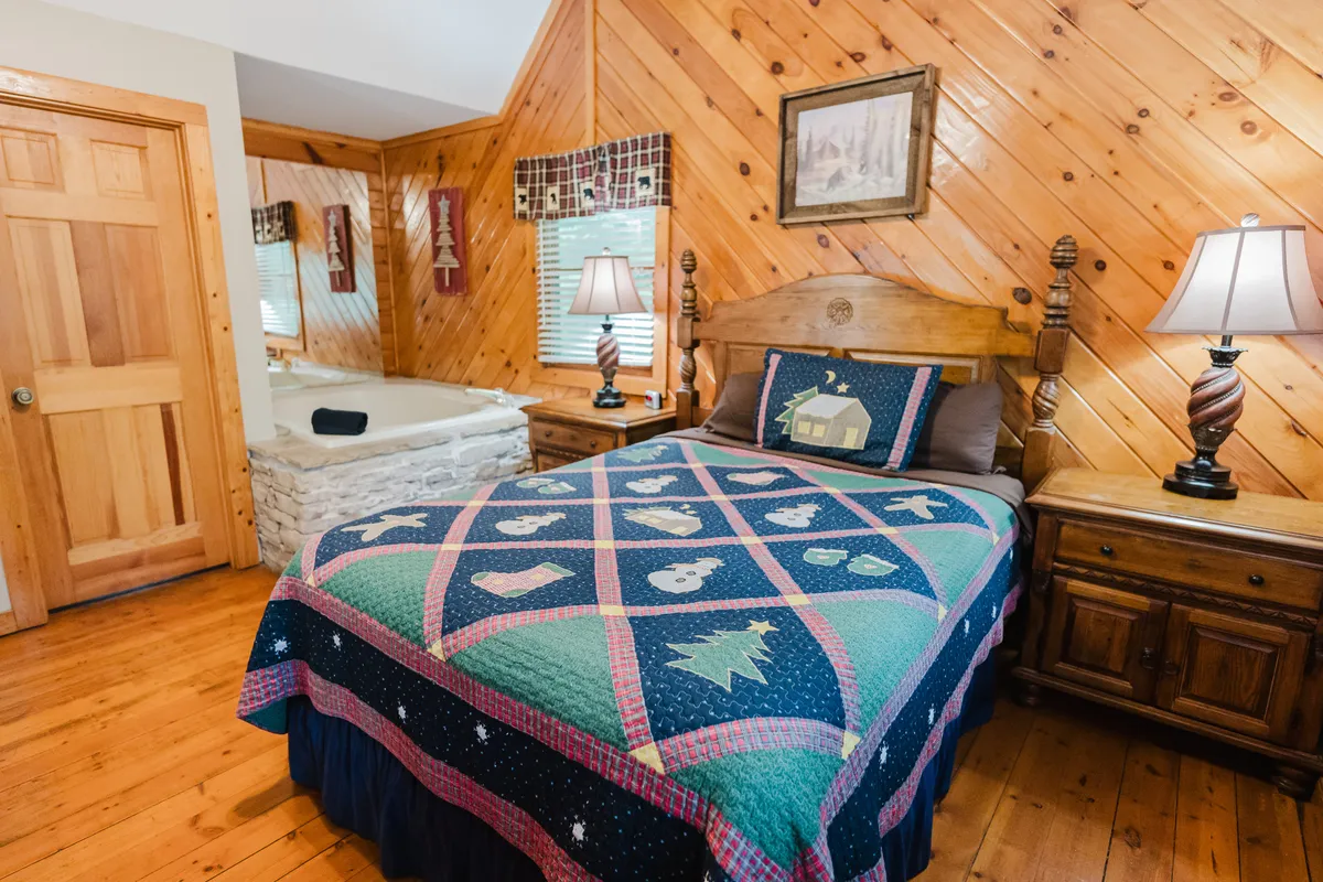 A comfortable bedroom scene with a plush bed covered in a quilt, a bathtub prominently situated nearby, and soft lighting from lamps. The wooden furniture and homey decor create a relaxing environment ideal for unwinding after a day of exploration or enjoying a soothing soak together.