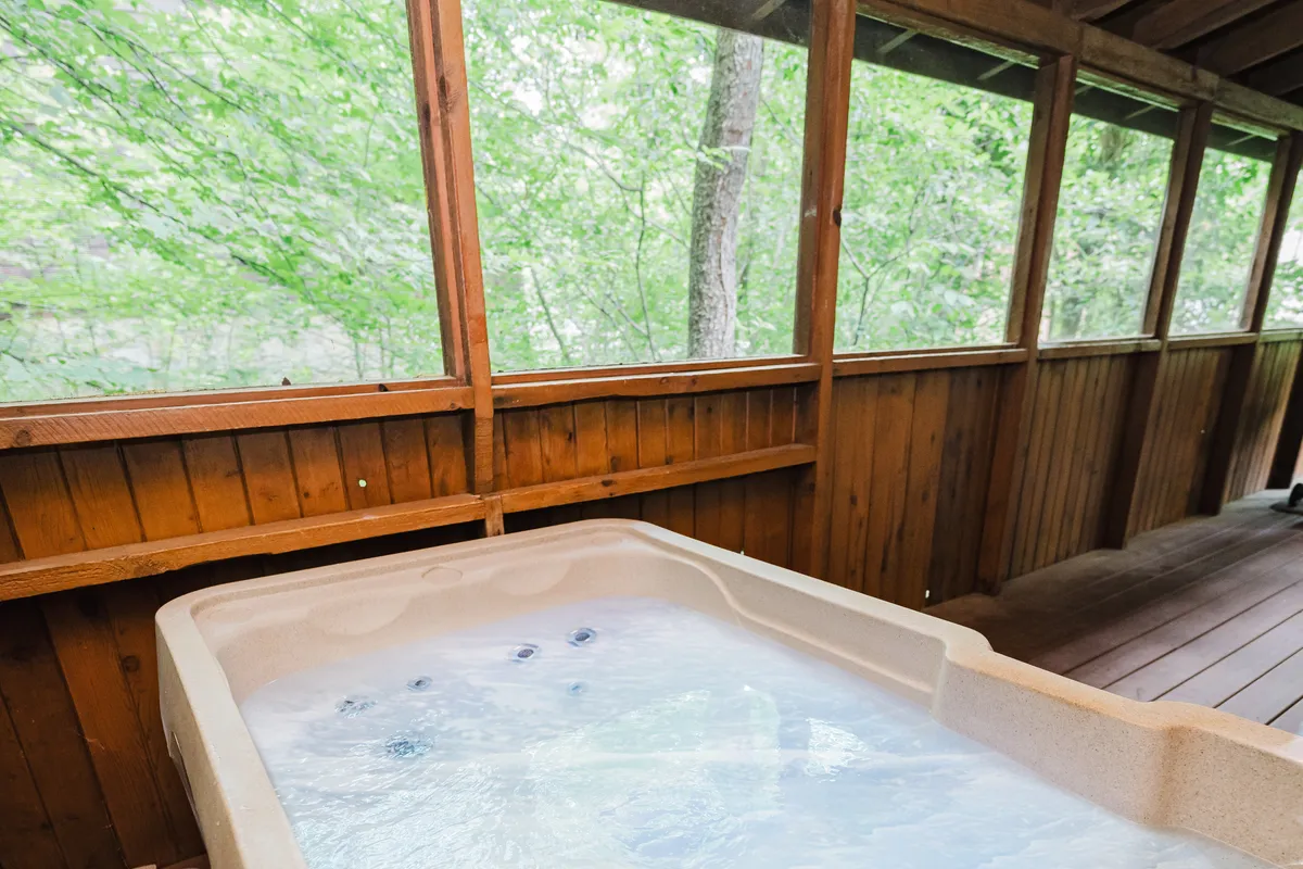 This image features a hot tub set against large windows with wooden paneling, allowing clear views of the surrounding nature. The tranquil atmosphere is emphasized by natural light streaming in, and the setup invites relaxation while connecting guests to the outdoors.