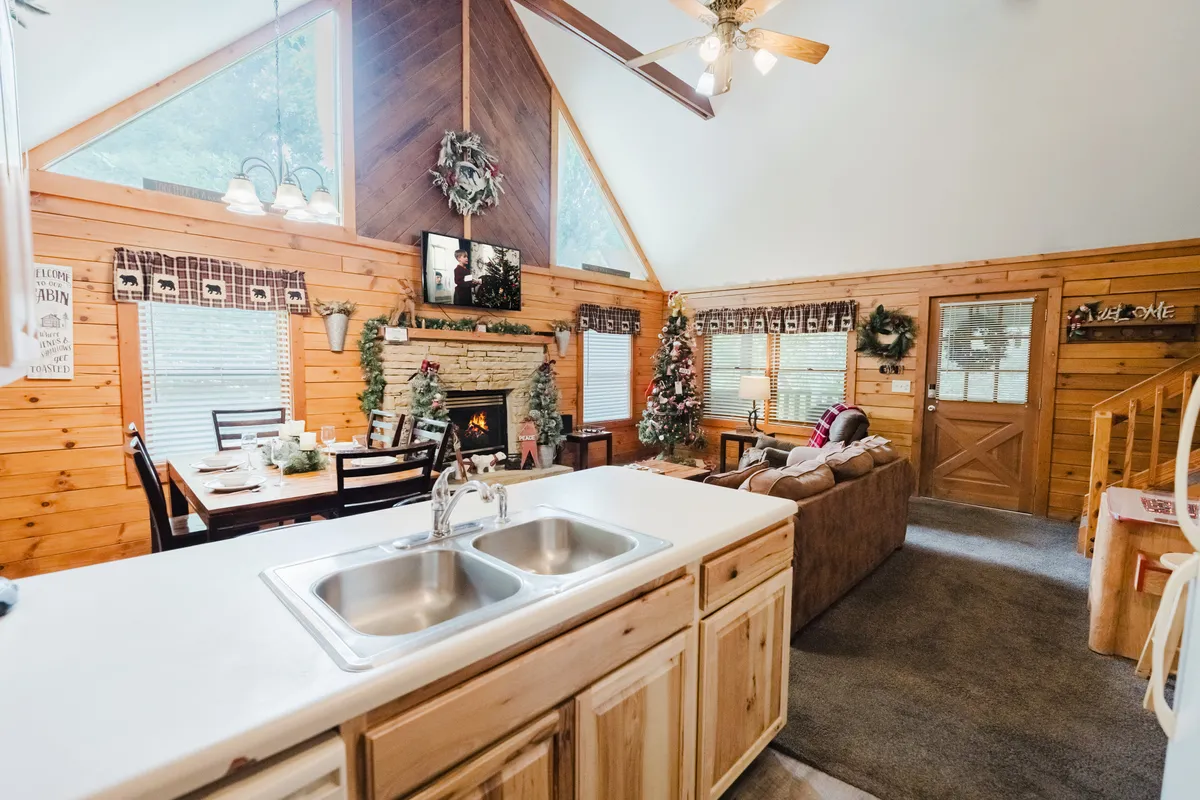 This image captures a warm and festive living area featuring a crackling fireplace, a Christmas tree sparkling with decorations, and a spacious dining table set for gatherings. Large windows fill the space with natural light, while the open layout encourages group activities and connection.