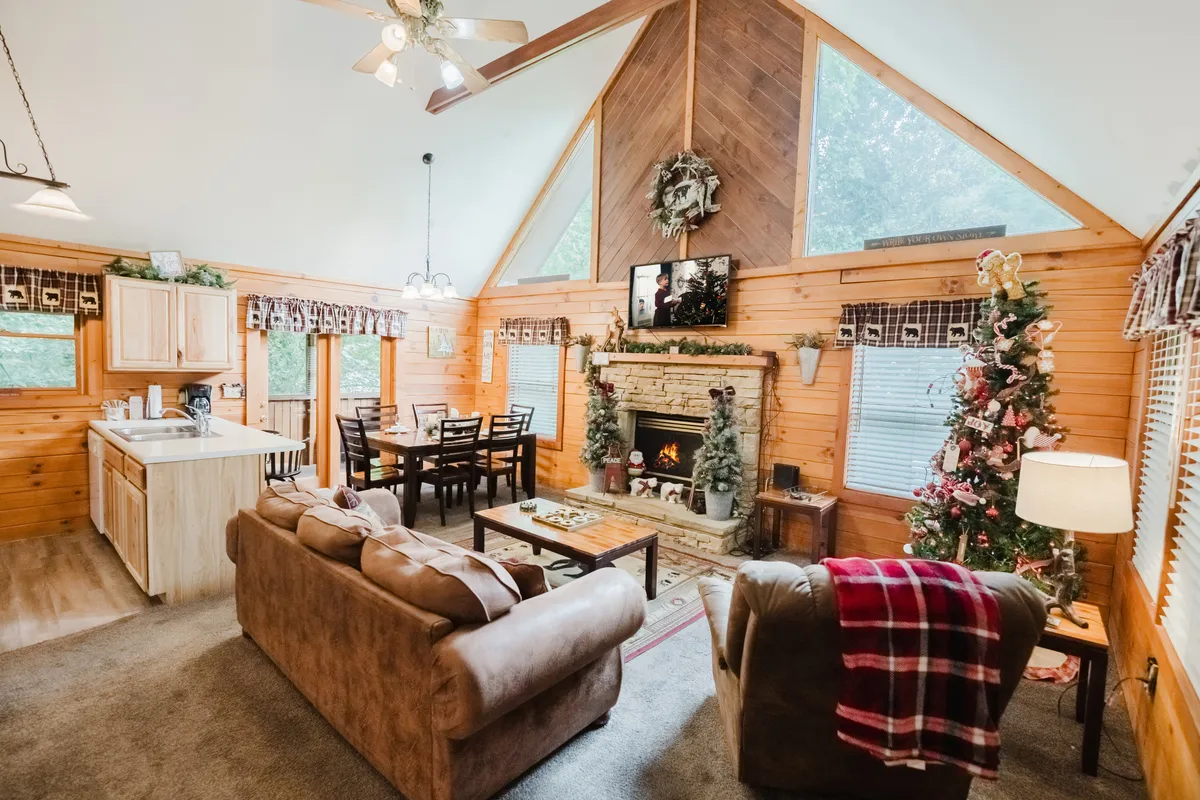 A wide view of the living area displays the fireplace, dining table, lush sofa, large windows, and a glowing Christmas tree. The space is filled with natural light, enhancing the welcoming and festive ambiance. Family gatherings, celebrations, and relaxation are depicted in a single, harmonious shot.