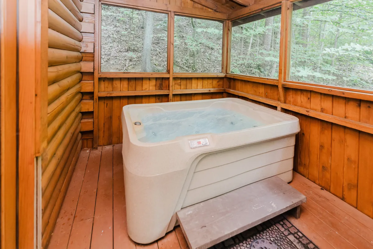 This image showcases an inviting hot tub inside a wood-paneled area with visible elements of the outdoors, including glimpses of greenery and natural light. The scene suggests both relaxation and a strong connection to the surrounding environment.