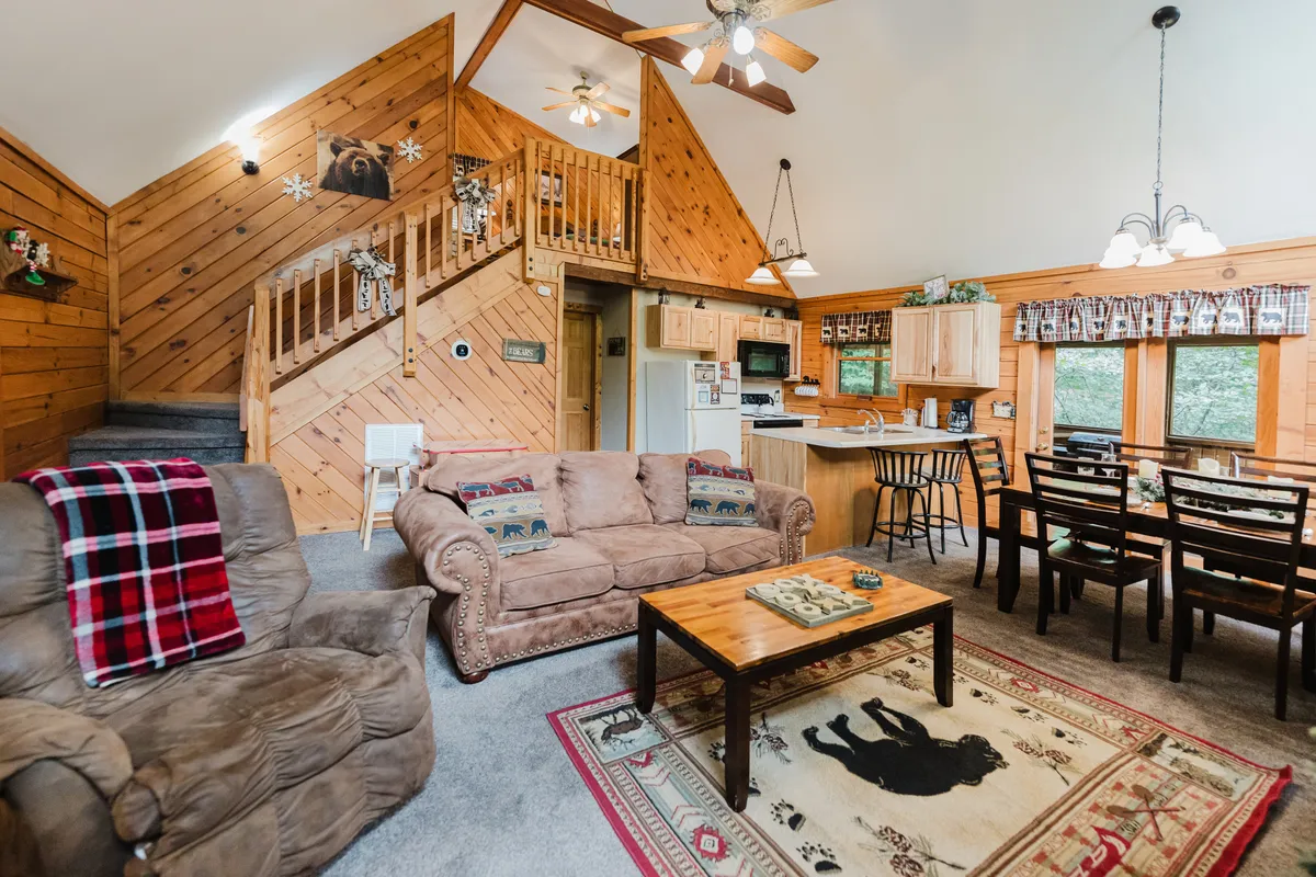 A spacious open-plan area featuring a welcoming dining table and a modern kitchen area. The scene includes a cozy sofa, wooden staircase, a dining table set for gatherings, and a fully equipped kitchen with ample counter space and appliances. Subtle holiday decor and warm lighting enhance the inviting, festive ambiance.