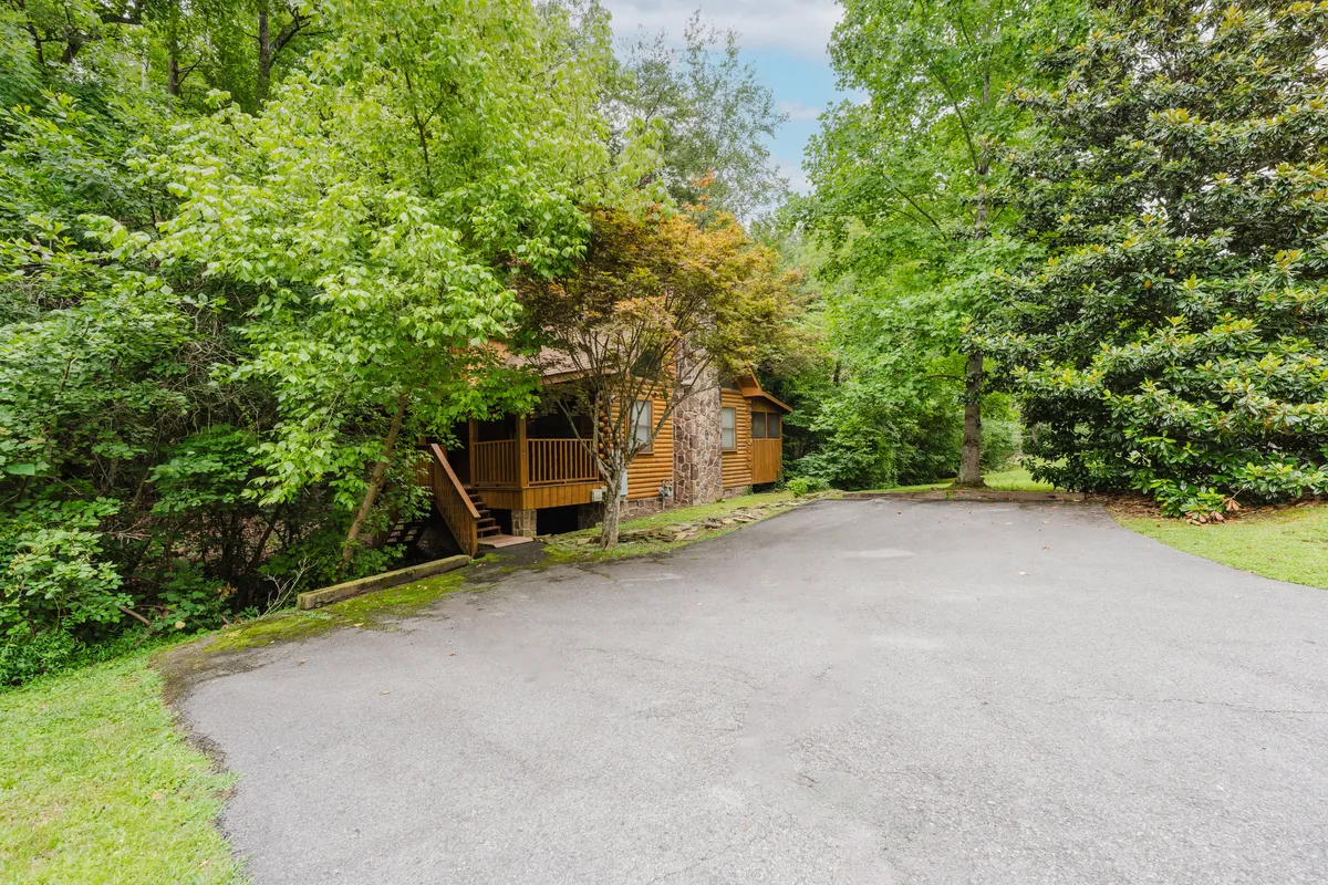 This image showcases the inviting exterior of a wooden house nestled among lush green foliage and stone features. The welcoming porch and surrounding nature evoke a sense of adventure and provide a visual connection to outdoor experiences just steps from the property.