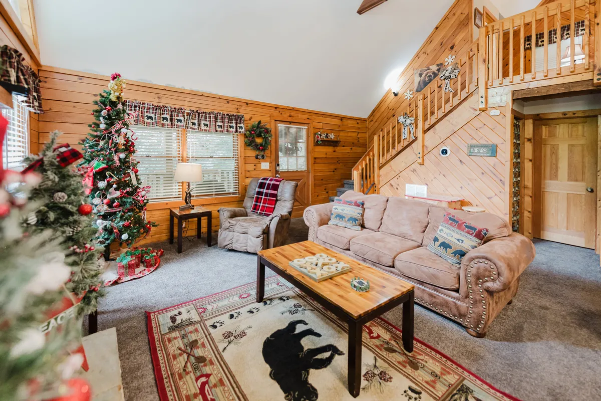 A cozy seating area is arranged around a beautifully decorated Christmas tree, complete with a plush sofa, coffee table, and a festive rug. The scene is filled with warmth, inviting guests to share stories, open presents, or simply enjoy each other's company in a holiday setting.