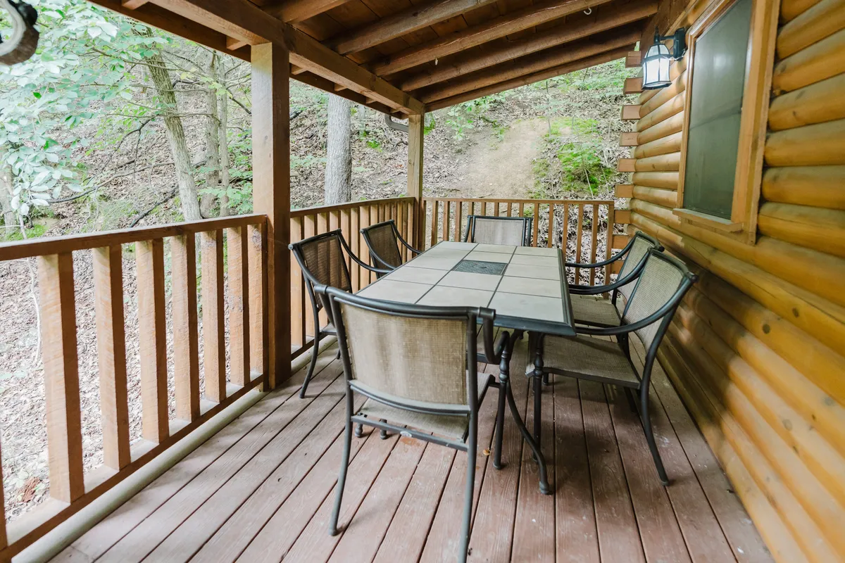An outdoor wooden dining table surrounded by lush trees and the log cabin structure, with comfortable seating for gatherings. The rustic deck provides a seamless transition between the festive interior and the enchanting Smoky Mountain surroundings.