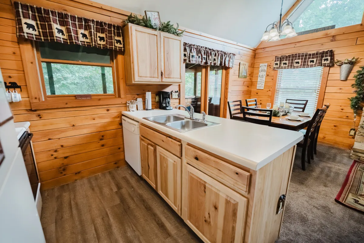 A bright and inviting kitchen with an island, wooden cabinetry, large windows letting in natural light, and a dining table nearby. The layout showcases modern appliances and a spacious prep area, perfect for cooking with loved ones or enjoying meals with scenic views.